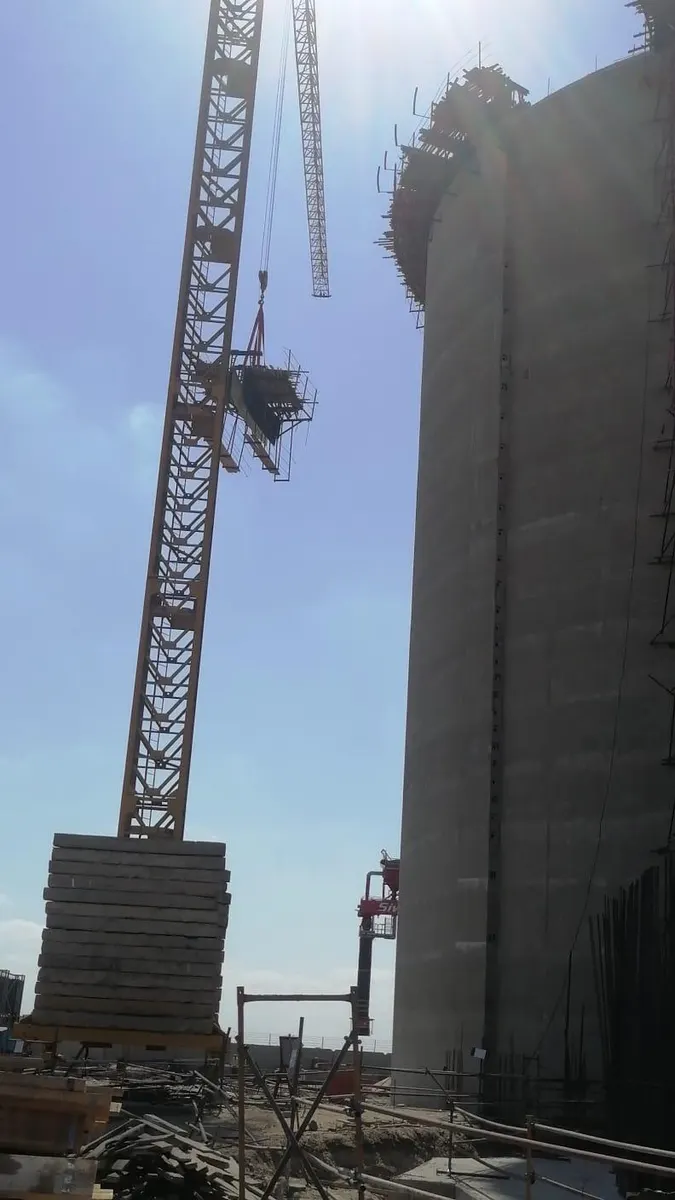 Tower crane lifting a formwork platform up the side of a silo under construction