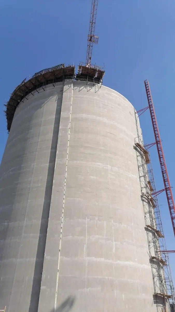 Low-angle view of a silo topped with roof formwork against a clear sky, with a crane mast alongside