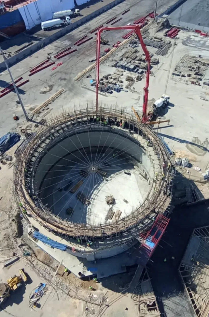 Aerial view of the silo roof pour, with a concrete pump boom reaching the top ring and the quay beyond